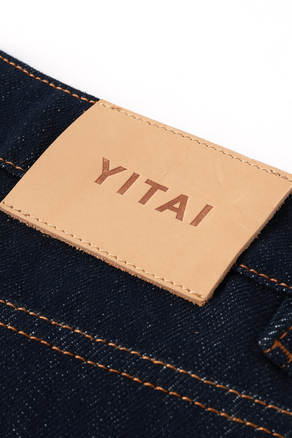 Close-up of a denim fabric with a tan leather label displaying 'YITAI'.