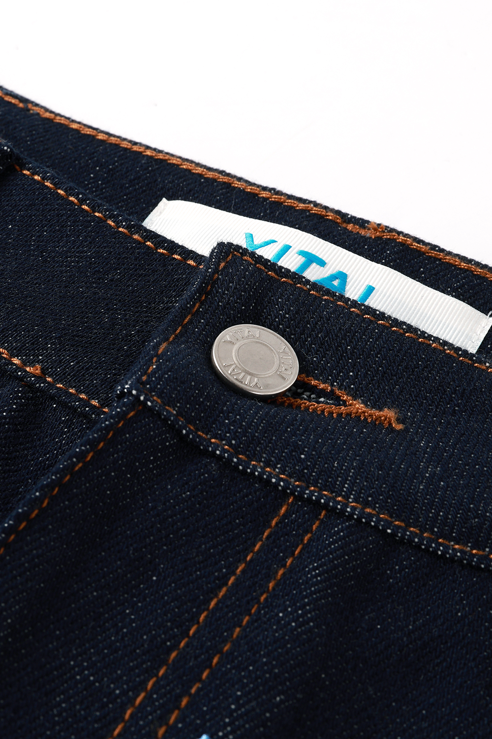 Close-up of a button on dark blue denim fabric with a brand label " YITAI"