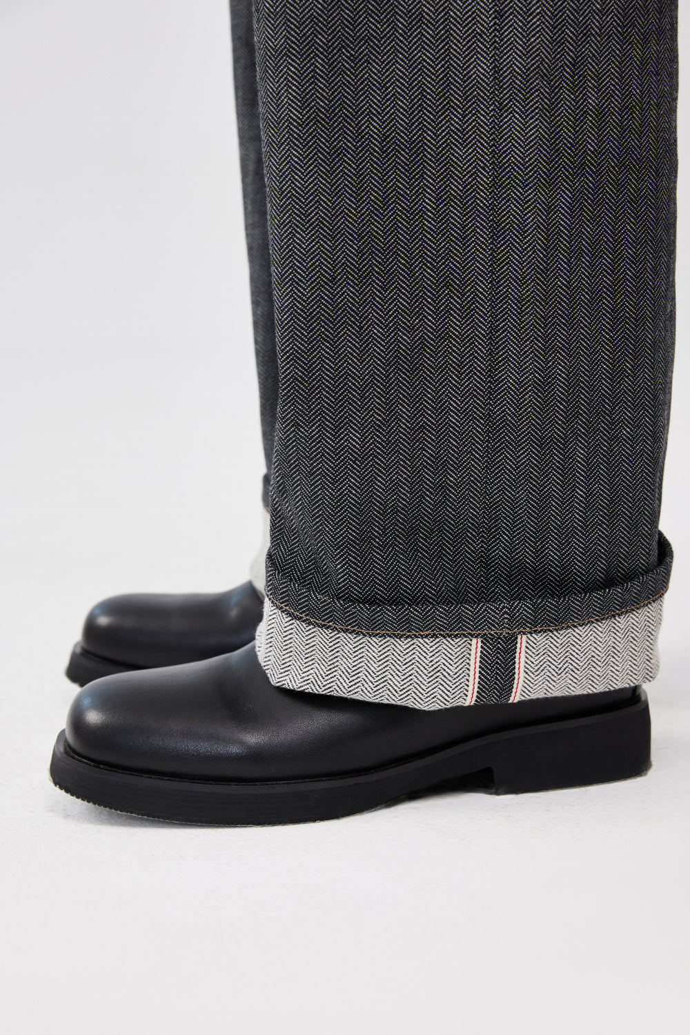 Close-up of grey herringbone selvedge denim jeans with rolled cuffs showing the selvedge edge.