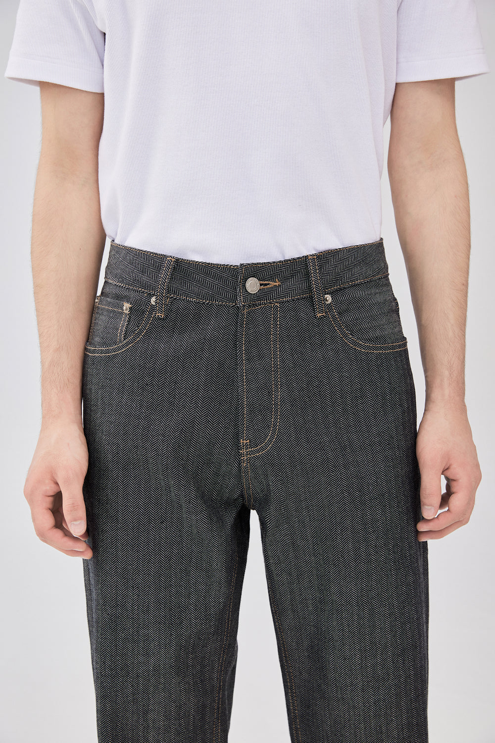 Close-up of grey herringbone selvedge straight-leg denim jeans showing the waistband, front pockets, and contrast stitching.