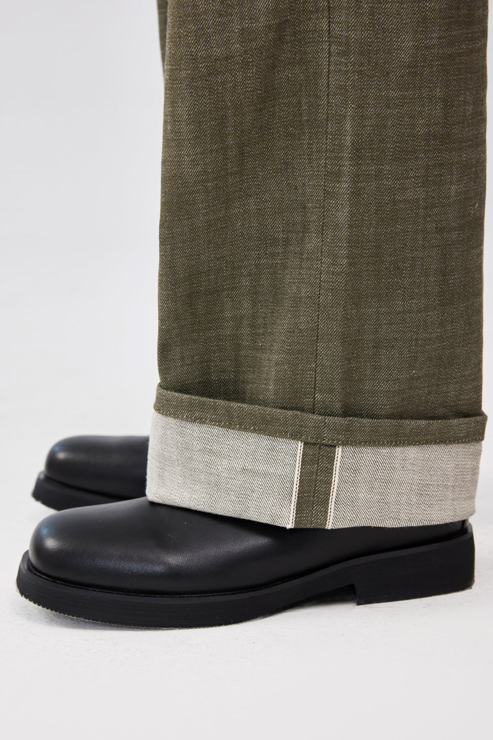 Close-up of military green selvedge denim jeans with rolled cuffs showing the selvedge edge.