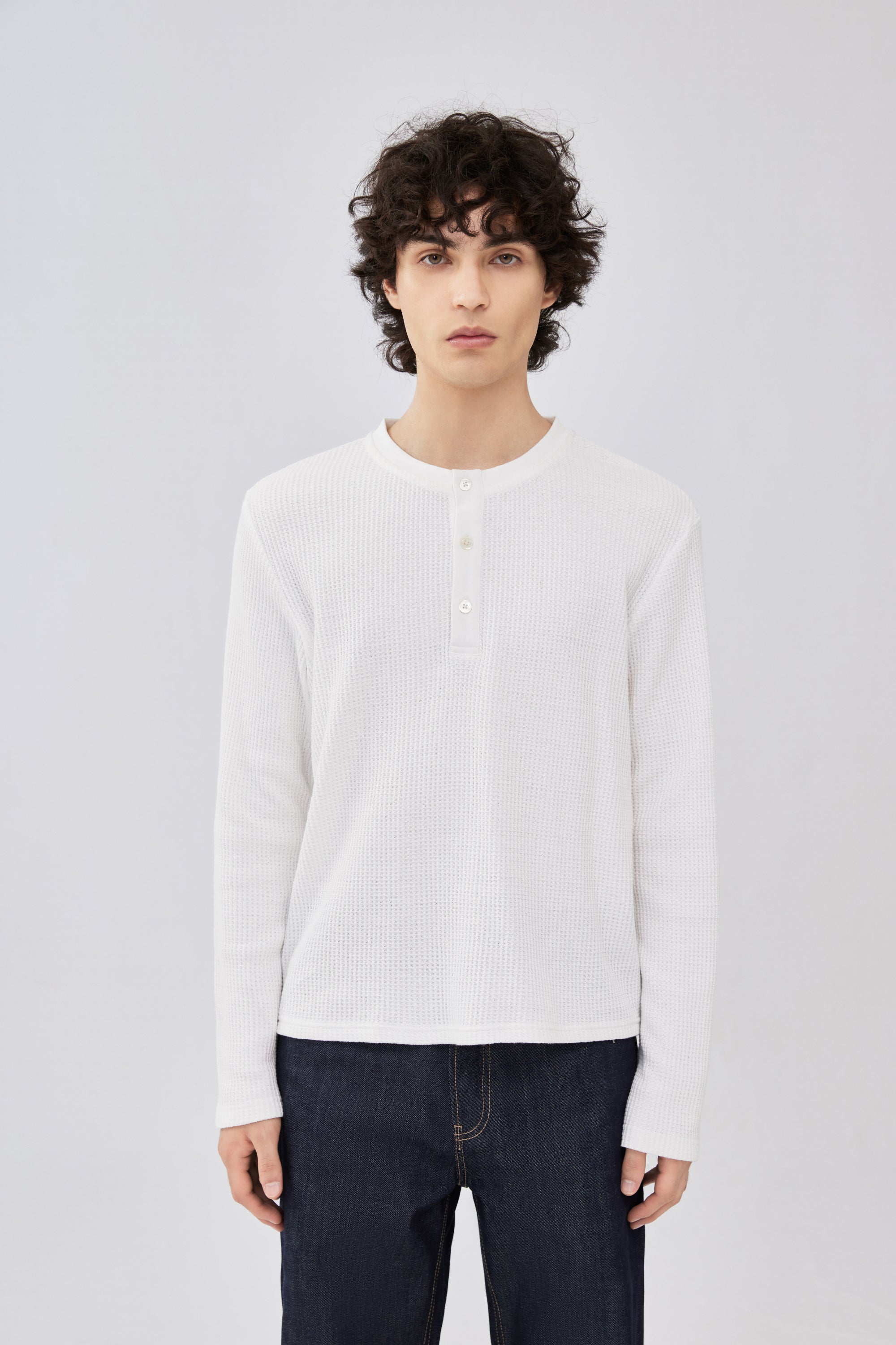 A male model wearing a white ribbed long-sleeve henley shirt and our Indigo Blue Selvedge Denim.