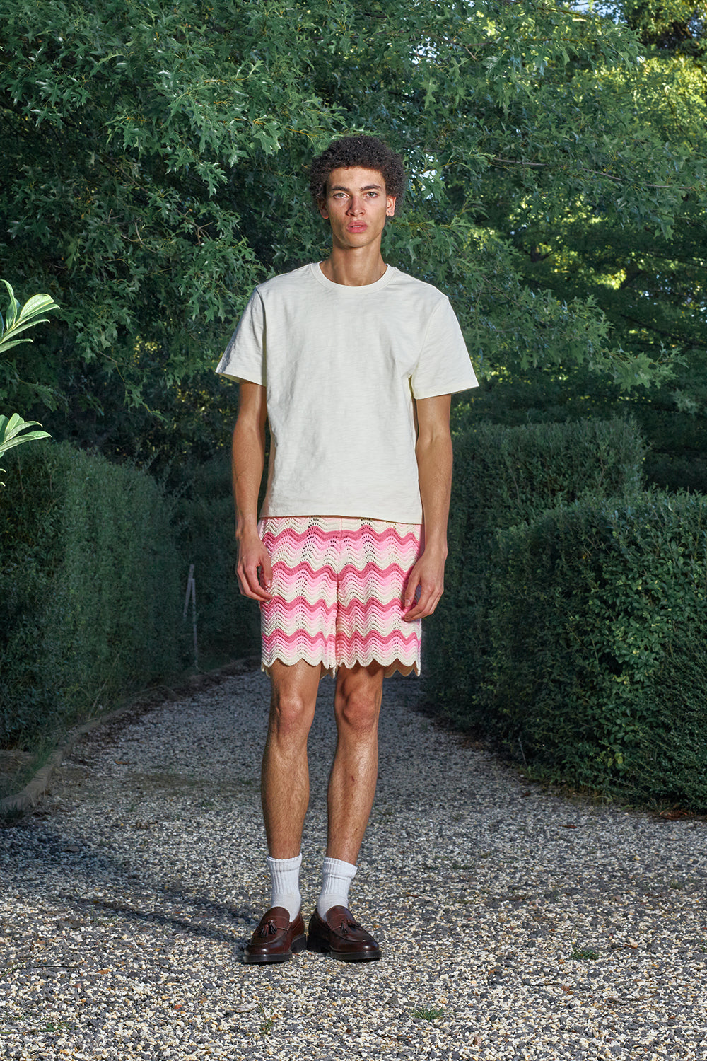 Model wearing pink and cream shale stitch knit shorts with a white T-shirt, standing outdoors.