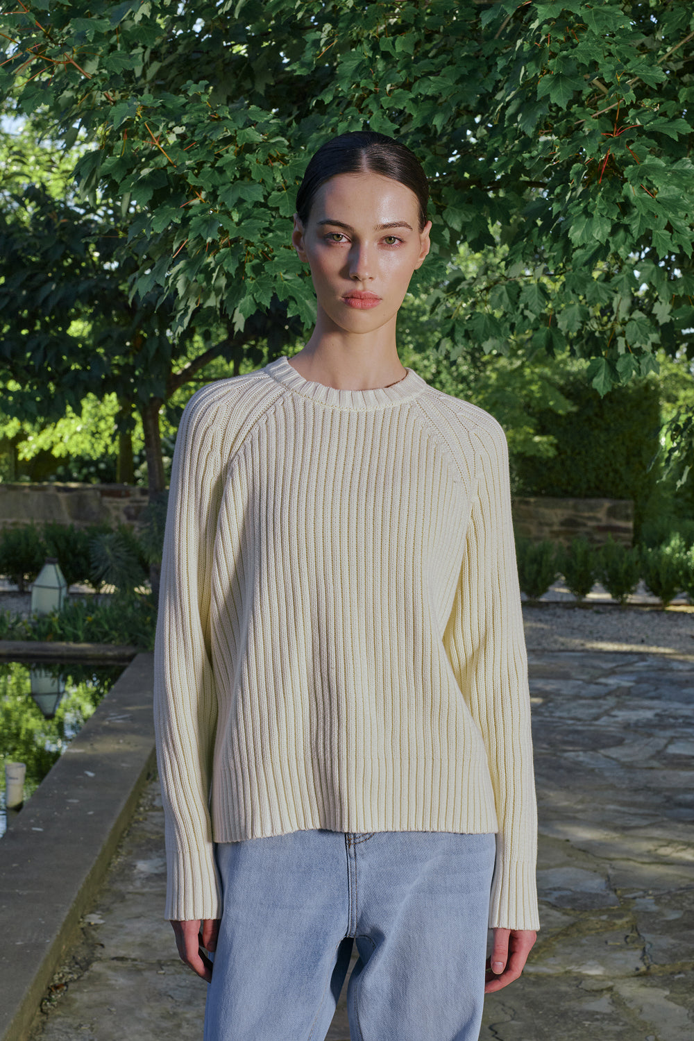 Close up for a model wearing a cream ribbed knit sweater with light jeans, standing outdoors.