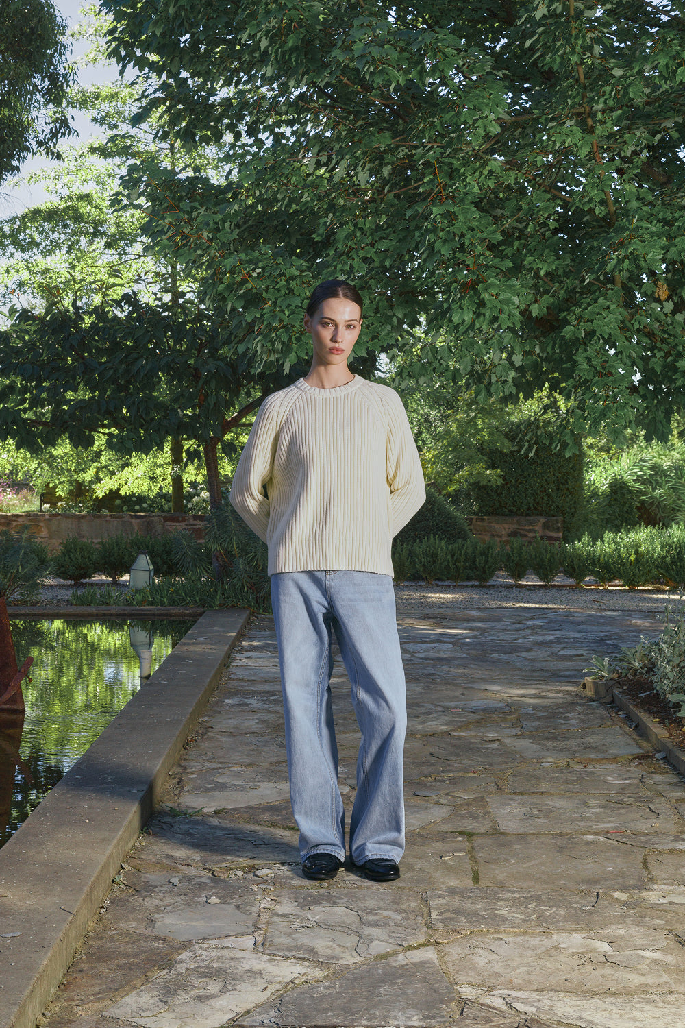 Model wearing a cream ribbed knit sweater with light jeans, standing outdoors.