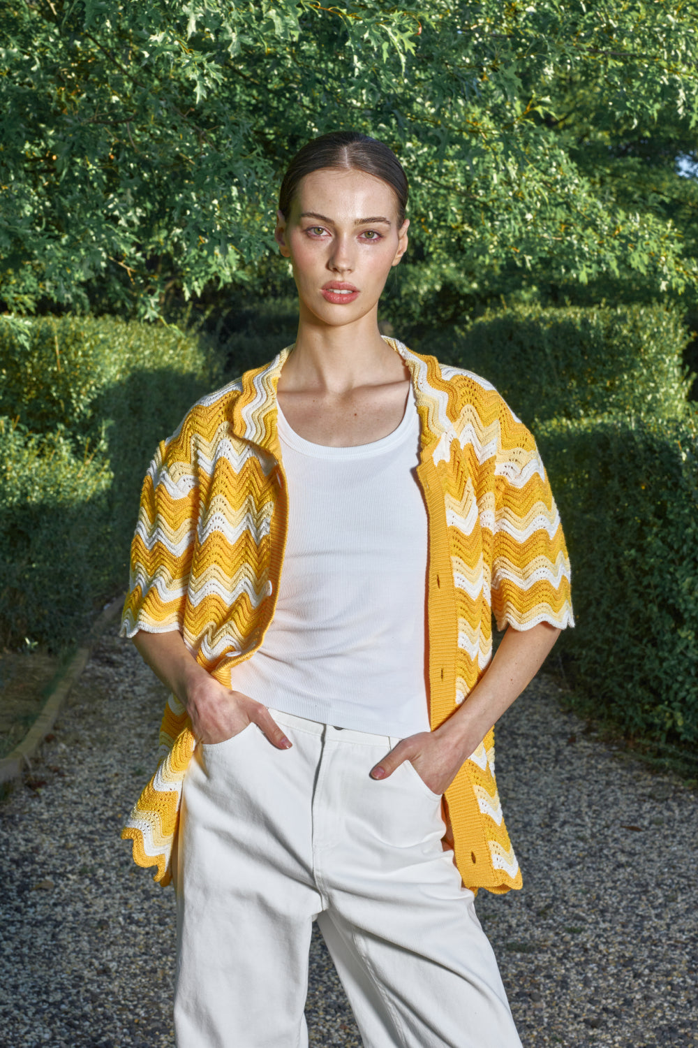 Model wearing a yellow and white shale stitch knit shirt over a white top and a white pants.