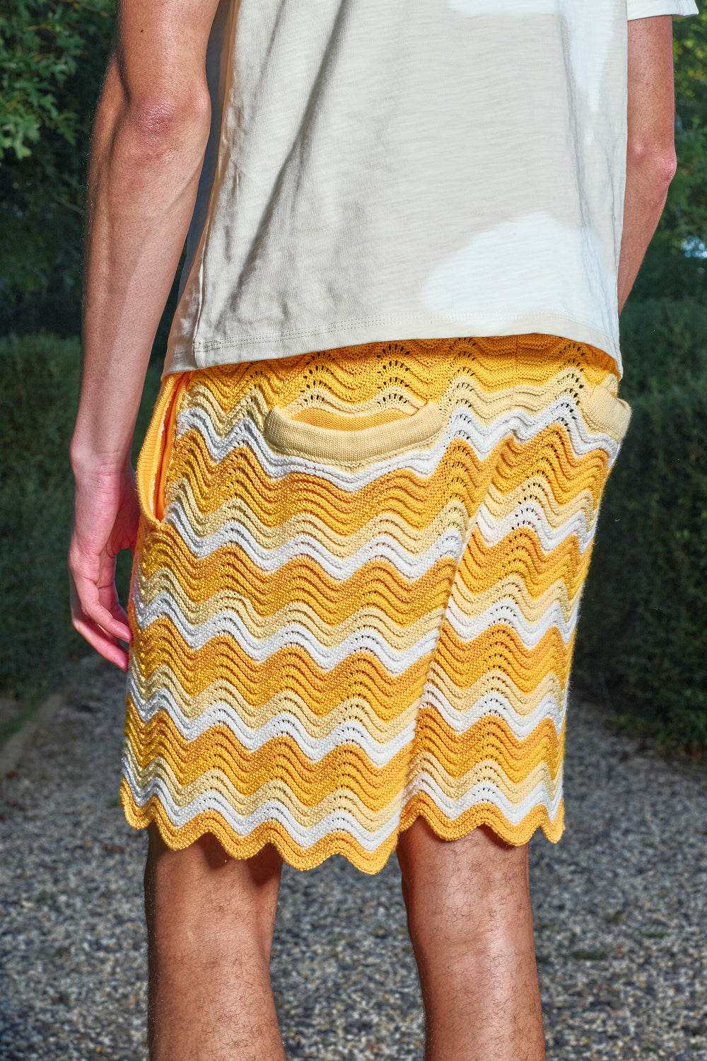 Close-up back view of model wearing yellow and white shale stitch knit shorts with back pockets.
