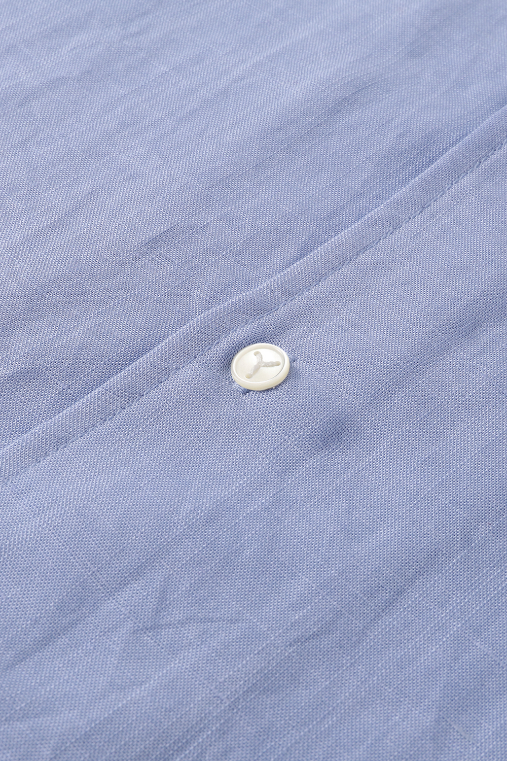 Close-up of a light blue textured fabric with a single white mother of pearl button.