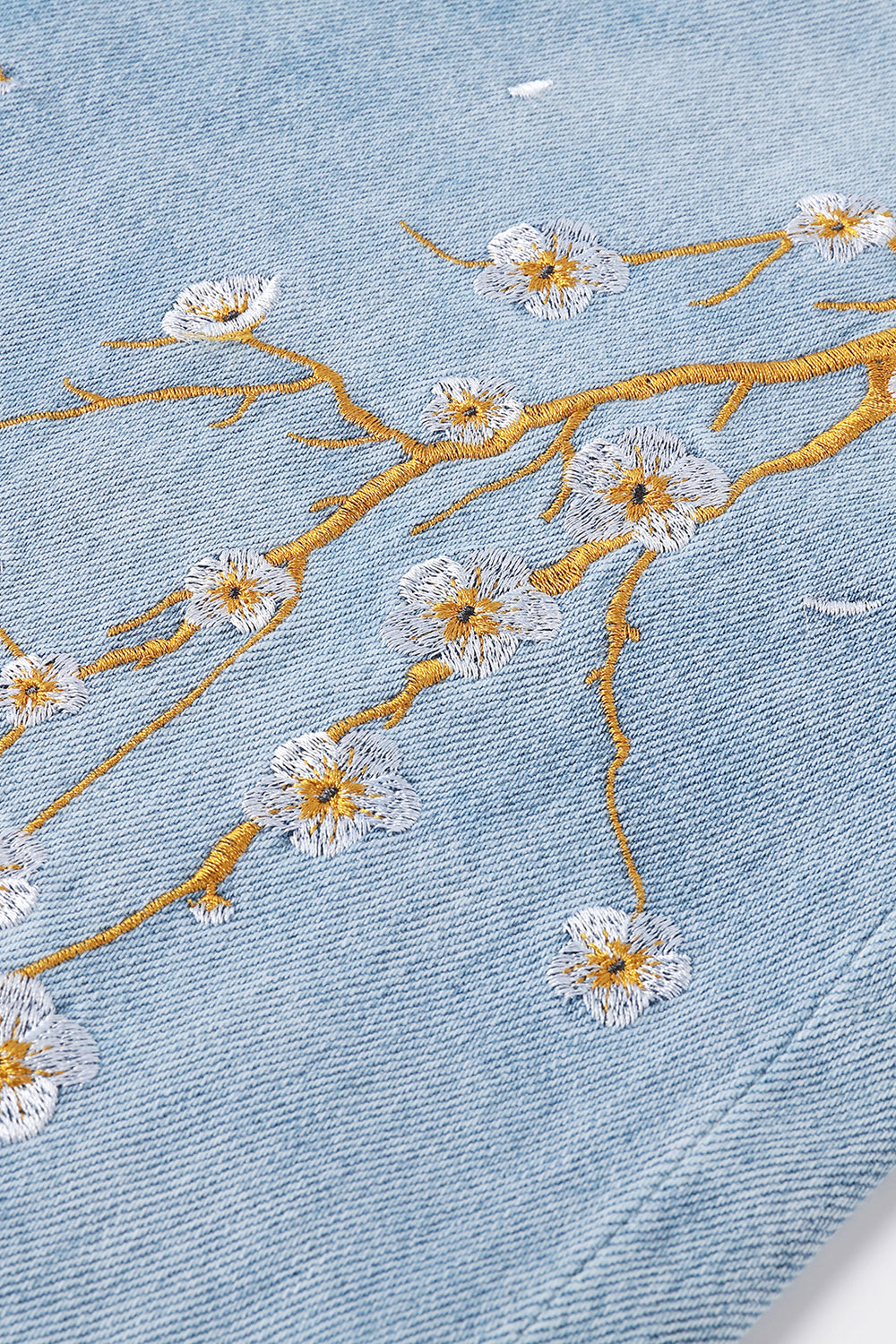 Embroidered floral design on denim fabric with gold thread.