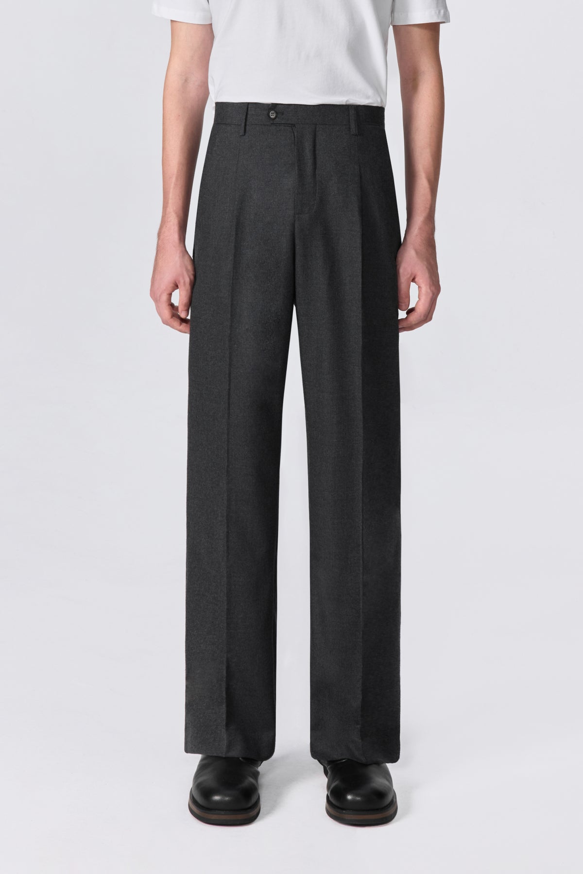 Full-length front view of model wearing charcoal pleated relaxed straight-leg fit wool trousers.