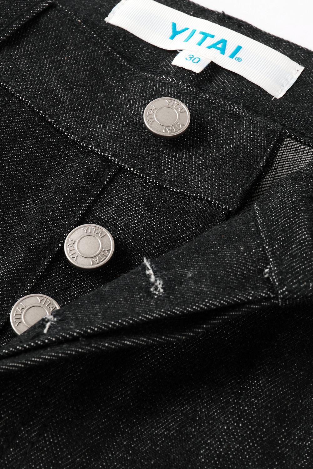 Close-up of black raw denim waistband showing YITAI branded rivet buttons and the size 30 fabric tag.