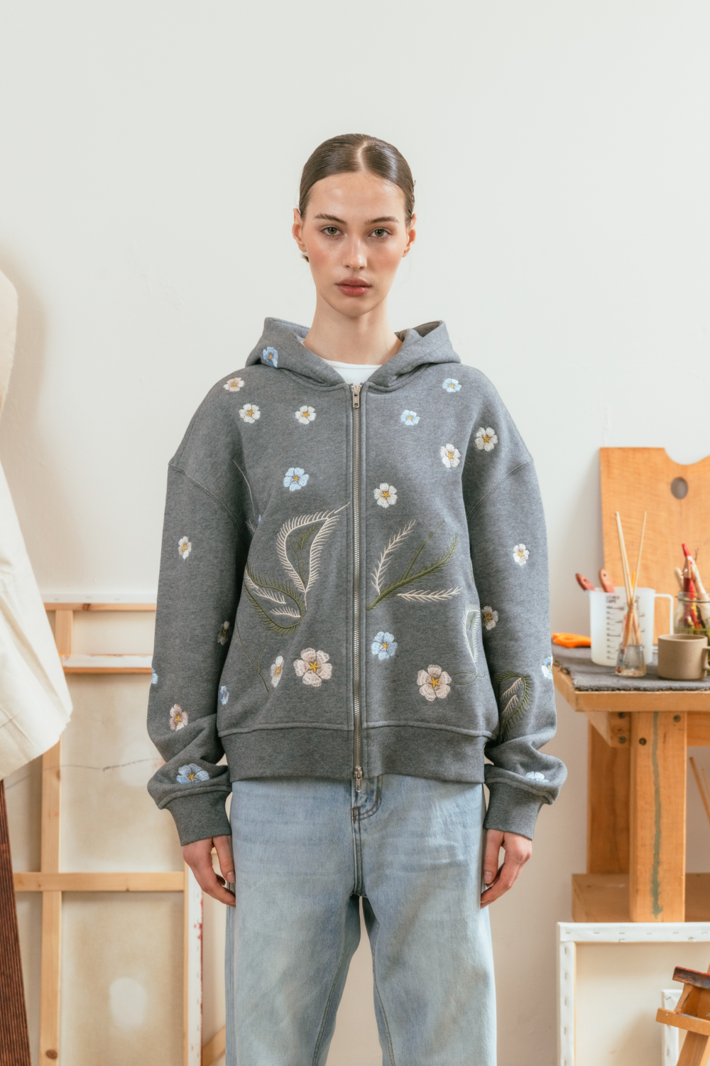 Person wearing a grey hoodie with floral embroidery in an indoor setting