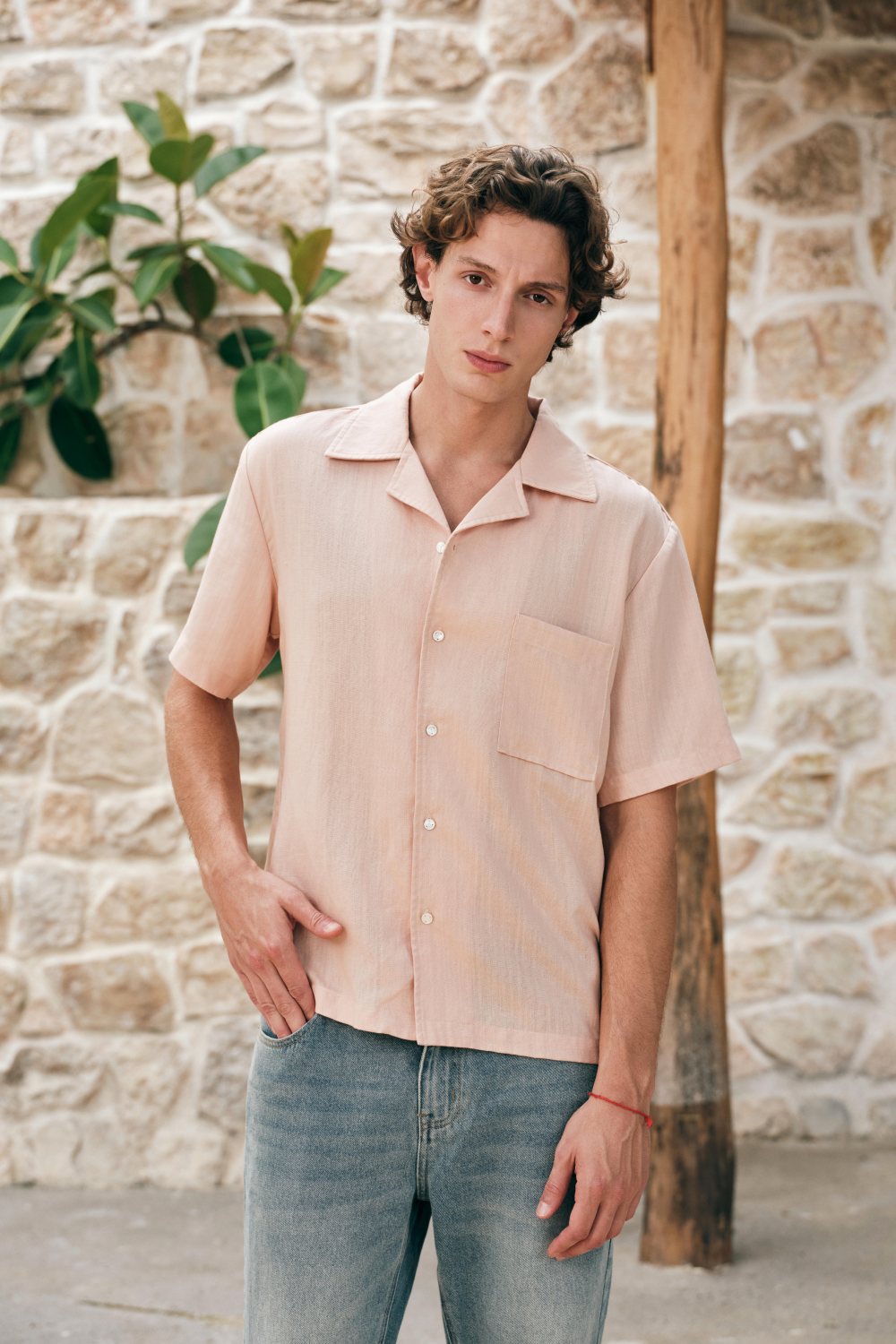 Model wearing a light pink short-sleeve button-up shirt with a camp collar and chest patch pocket.