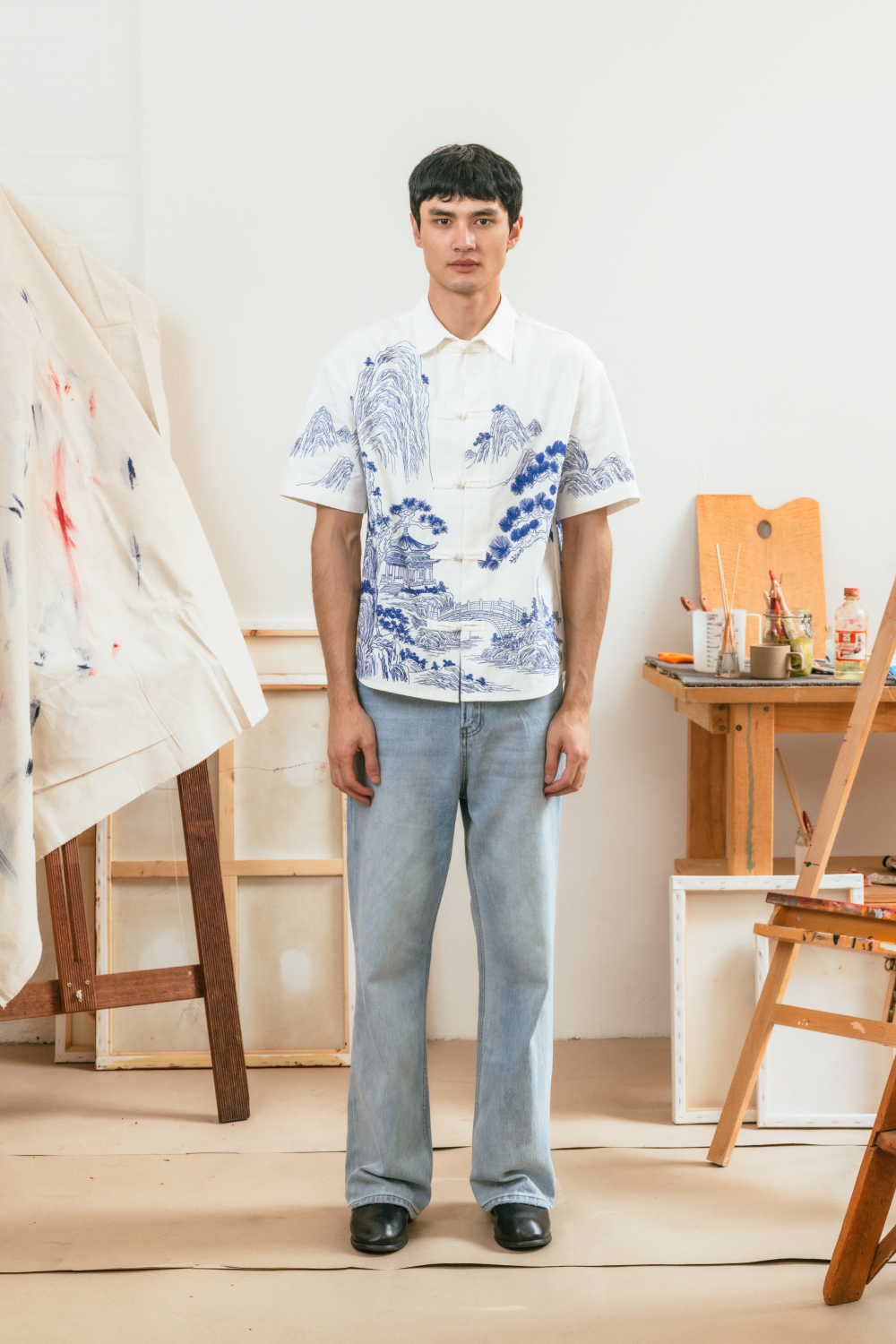 Man wearing a white shirt with traditional blue embroidery and light blue jeans in an art studio.