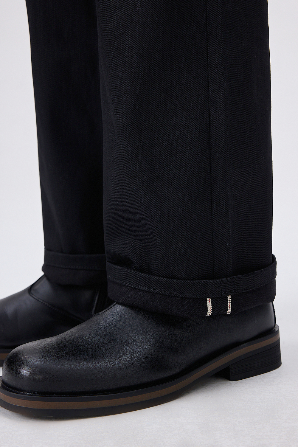 Close-up of black selvedge denim cuffs with signature selvedge detail, paired with black leather boots.