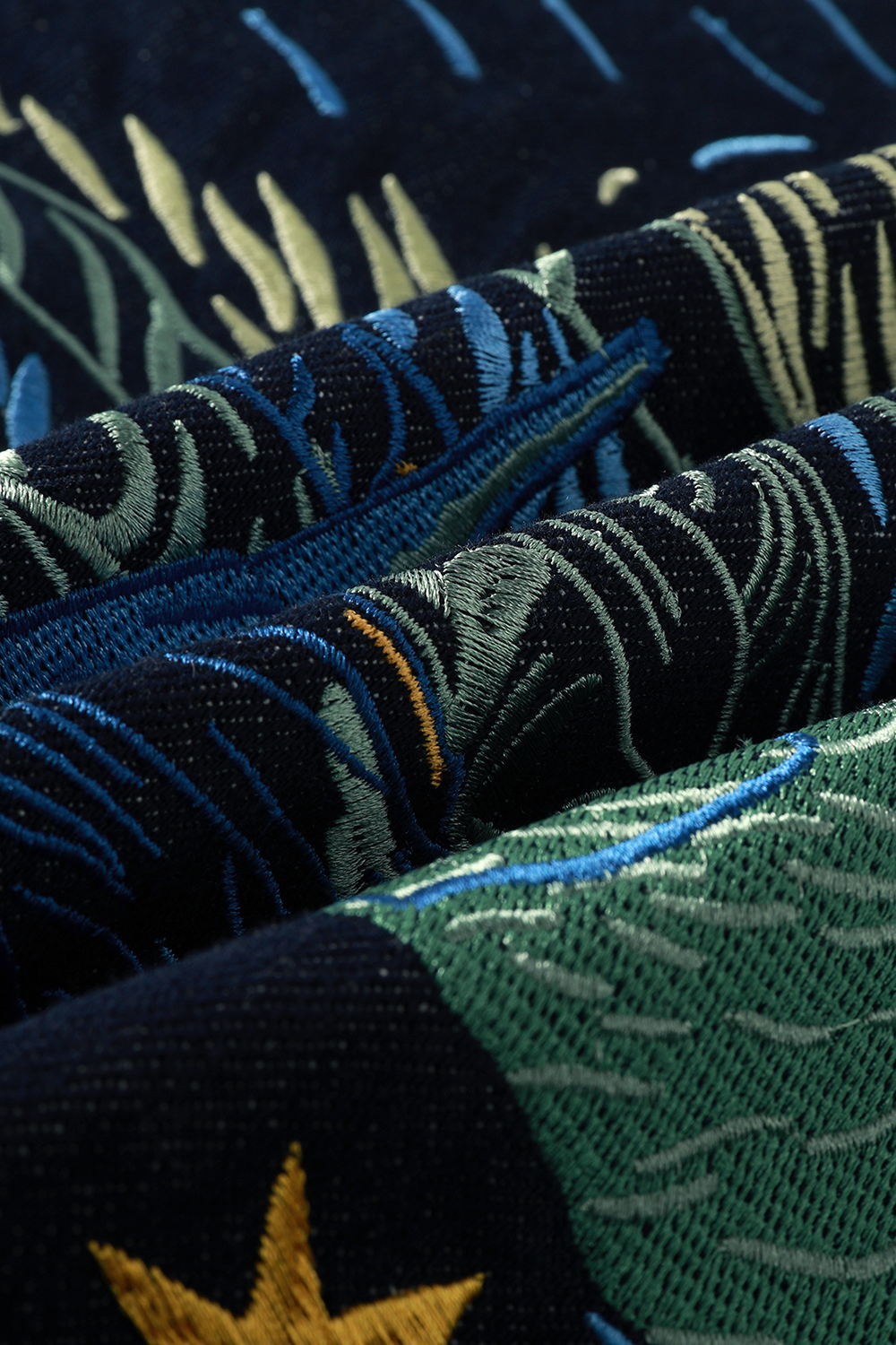Close-up of dark denim with Starry Night-inspired embroidery in shades of blue, green, yellow, and cream.