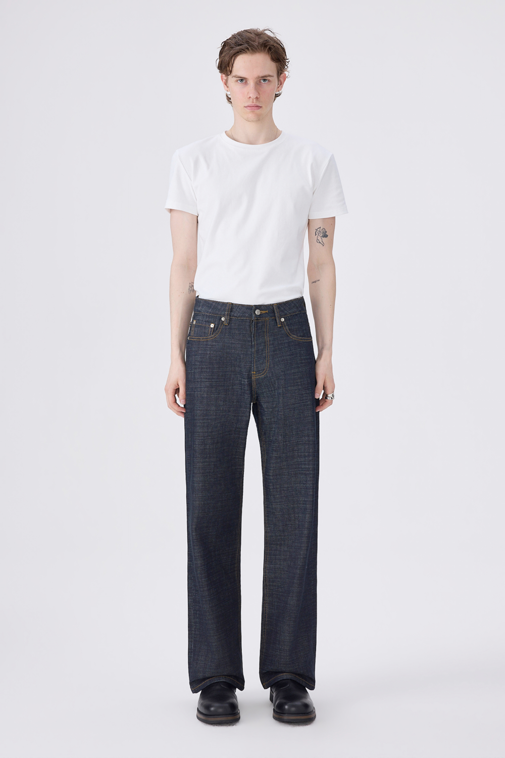 Full-length front view of a model wearing dark indigo selvedge denim jeans with contrast gold stitching and a straight-leg fit.