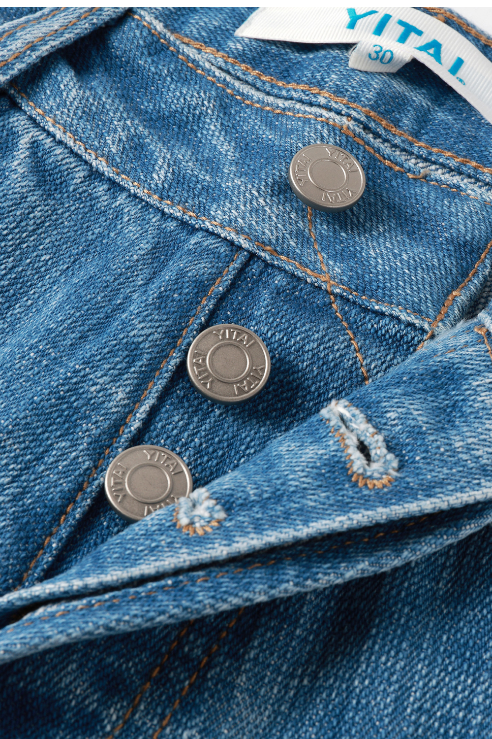 Close-up of light-wash denim waistband showing YITAI branded rivet buttons, contrast tan stitching, and the size 30 fabric tag.