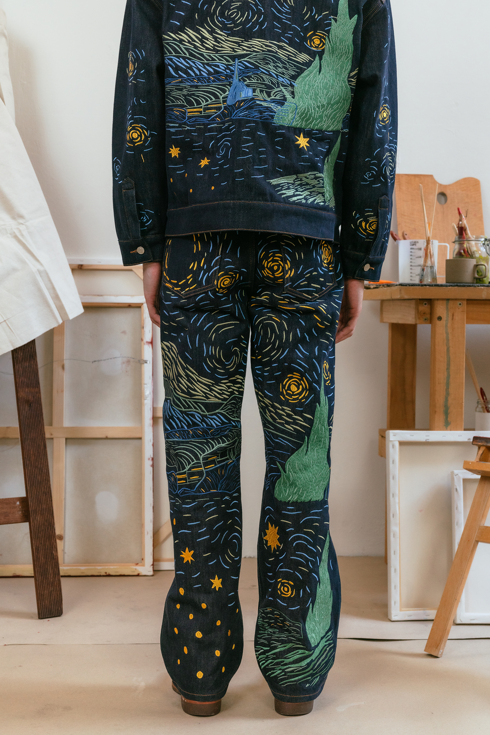 Back view of a model wearing a matching Starry Night-inspired denim jacket and jeans set with blue and yellow embroidery.
