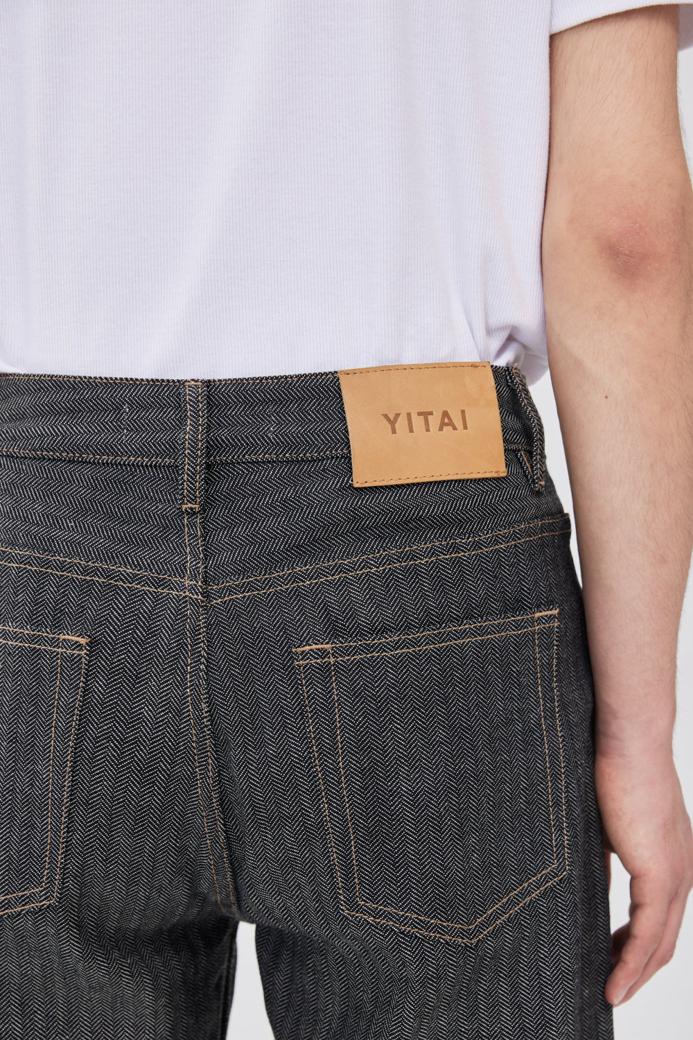 Close-up of the back waistband of grey herringbone selvedge denim jeans with a tan leather YITAI brand patch.