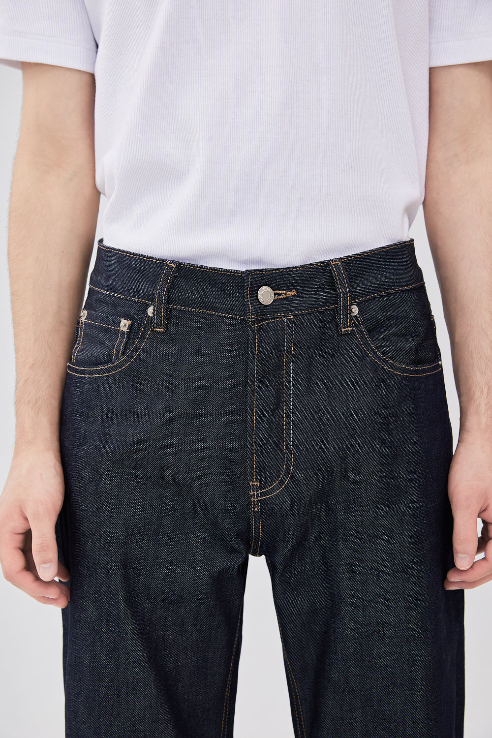 Close-up of a person wearing dark indigo blue denim jeans with contrast tan stitching.