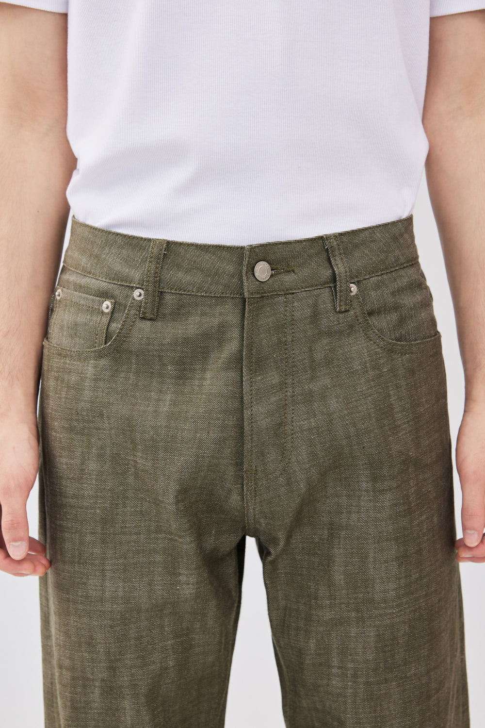 A close-up of a model wearing military green selvedge denim jeans showing the front waistband, belt loops, and front pockets.