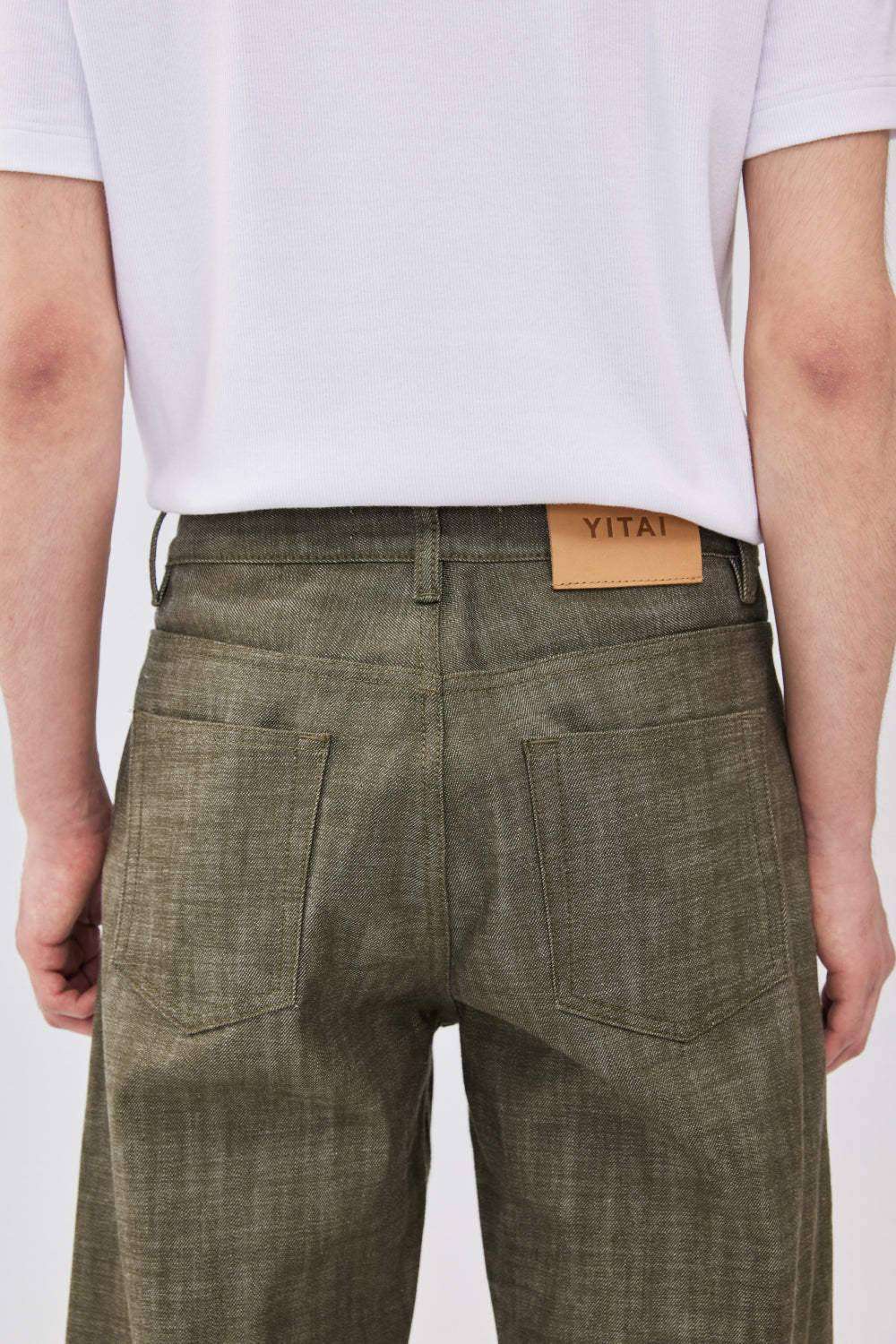 Close-up of the back waistband of military green selvedge denim jeans with a tan leather YITAI brand patch.