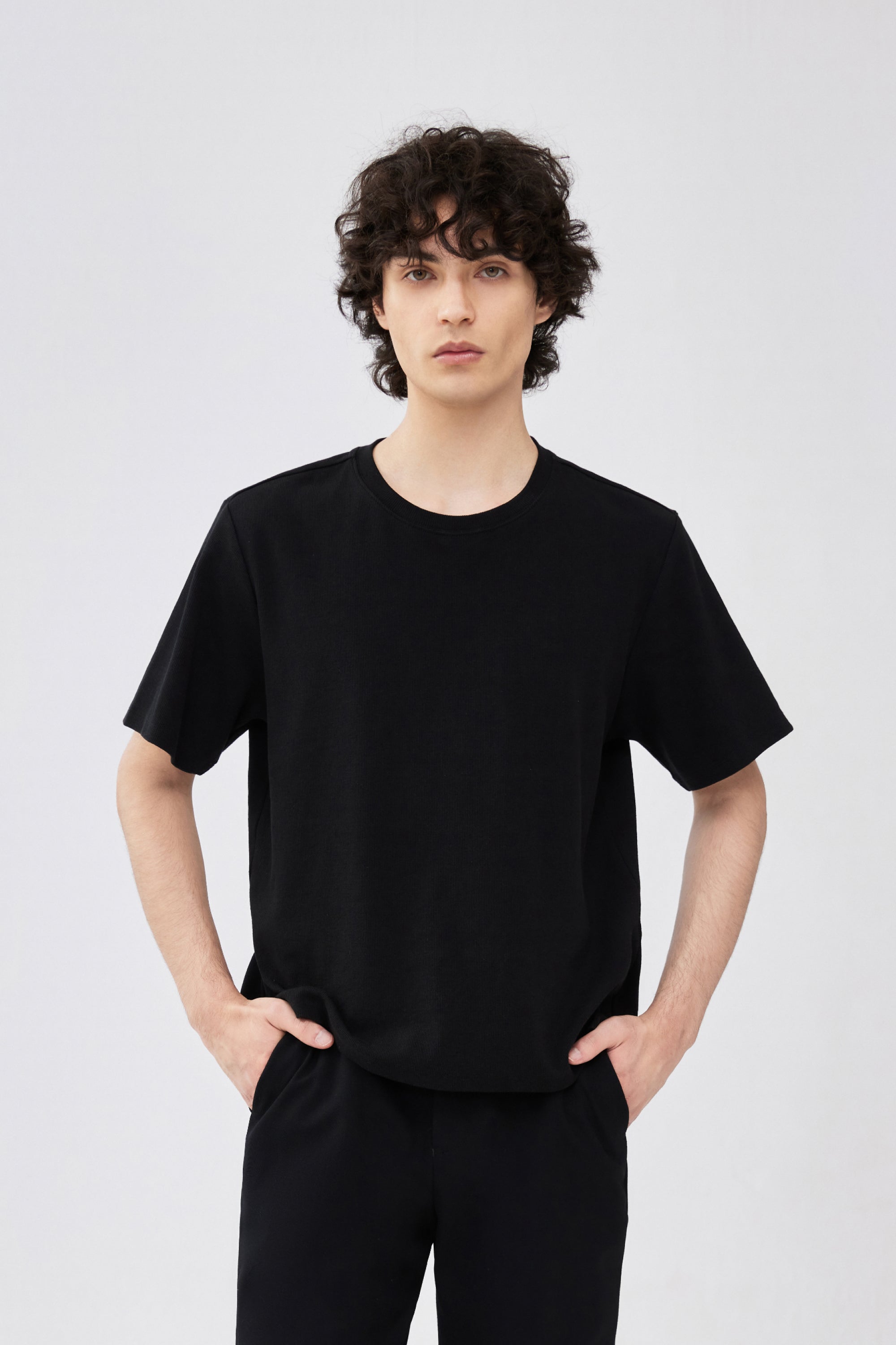 A model wearing a plain black ribbed short-sleeve crewneck t-shirt and black pants.