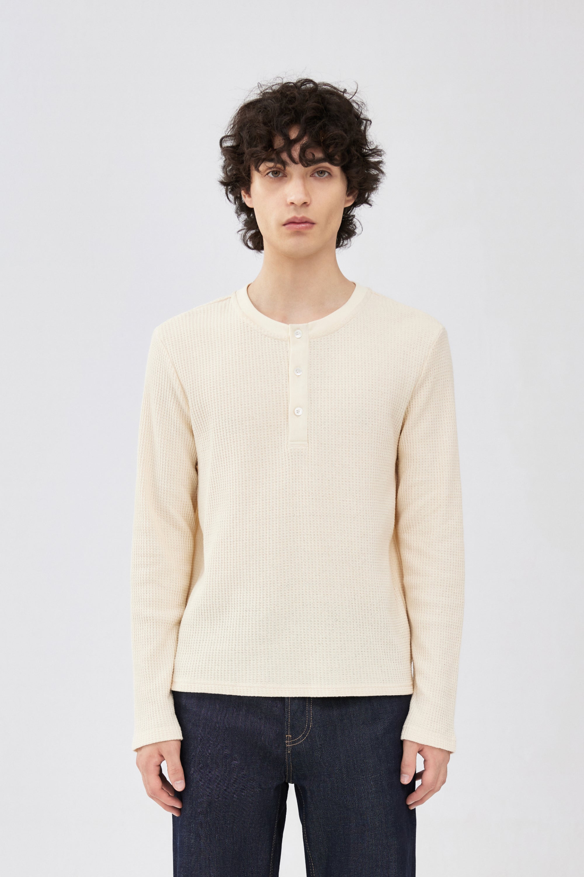 A male model wearing a cream-colored ribbed knit henley sweater with our Indigo Blue Selvedge Denim.
