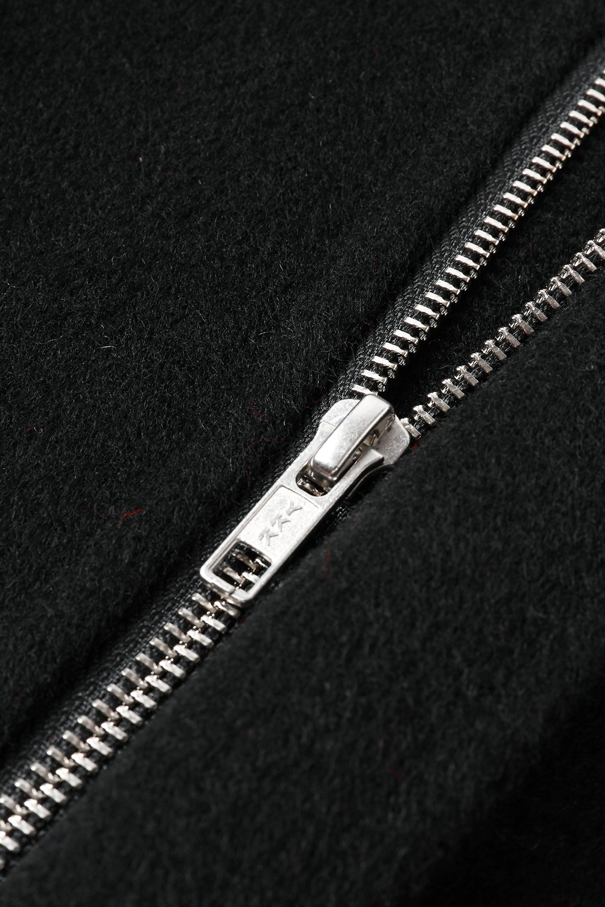 Close-up of a silver metal YKK zipper pulled open on a black wool and cashmere fabric surface.